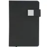Toma fotográfica de libretas promocionales con cubierta rígida en color negro, broche magnético lateral con placa metálica cuadrada y sujetador para bolígrafo ideal para grabado de marca.
